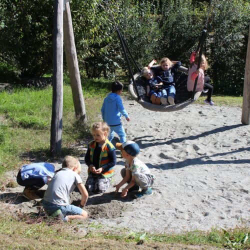 Kinder schaukeln und spielen im Sand